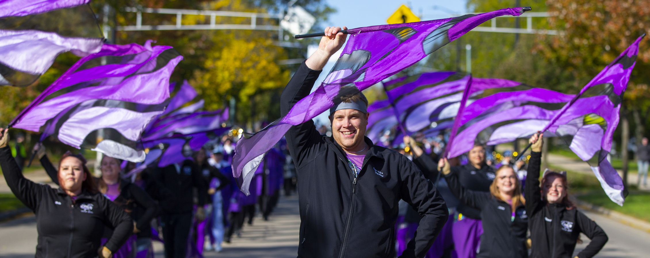 The Color Guard marches in the parade with purple flags in the air.